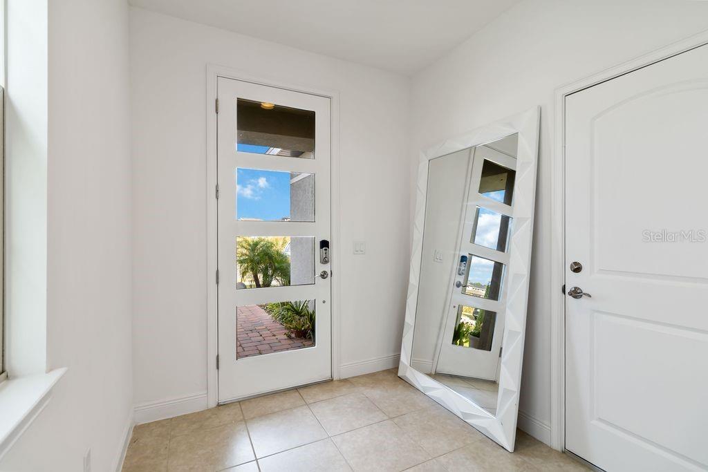 An entryway features a white door with glass panels, a large geometric mirror, and tile flooring — 3212 OXBOW COURT, HARMONY, FL