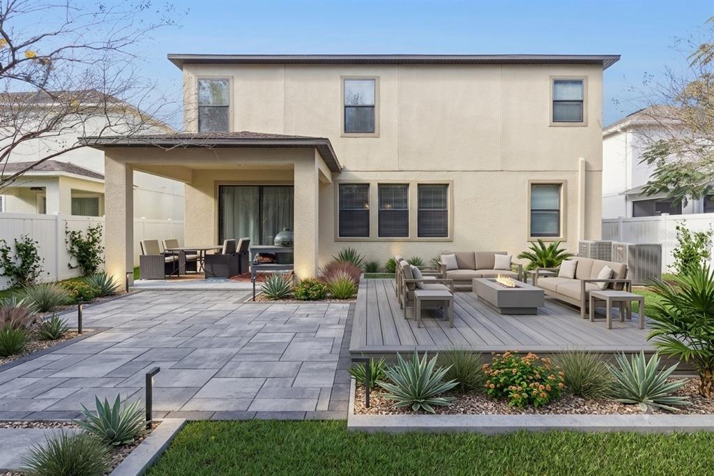 A backyard features a paved patio, a wooden deck with a fire pit, and landscaping — 8816 SHADY PAVILLION COURT, LAND O LAKES, FL