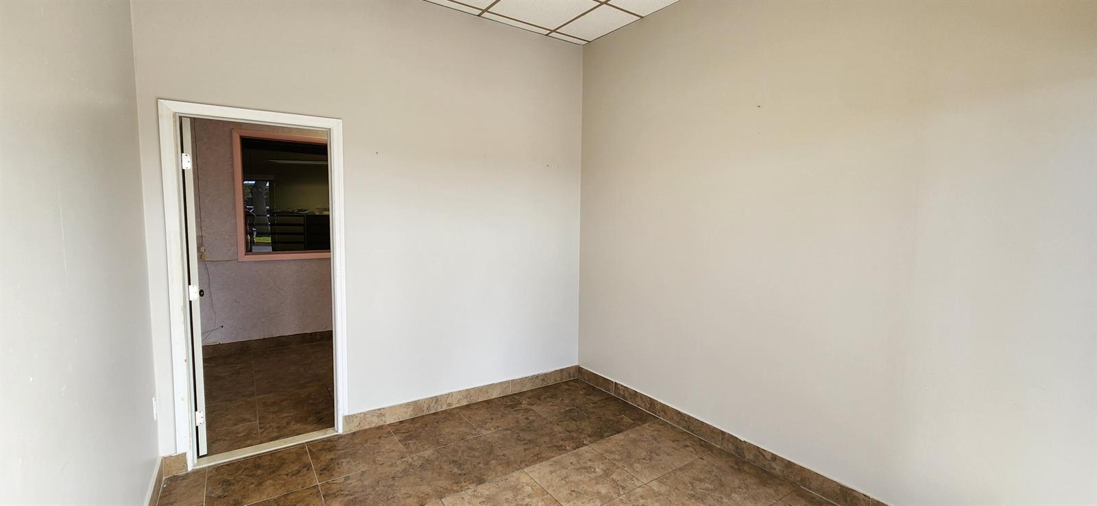 An empty room with beige walls, brown tile flooring, and a doorway leading to another space — 1207 S Powerline Road, Pompano Beach FL 33069, POMPANO BEACH, FL