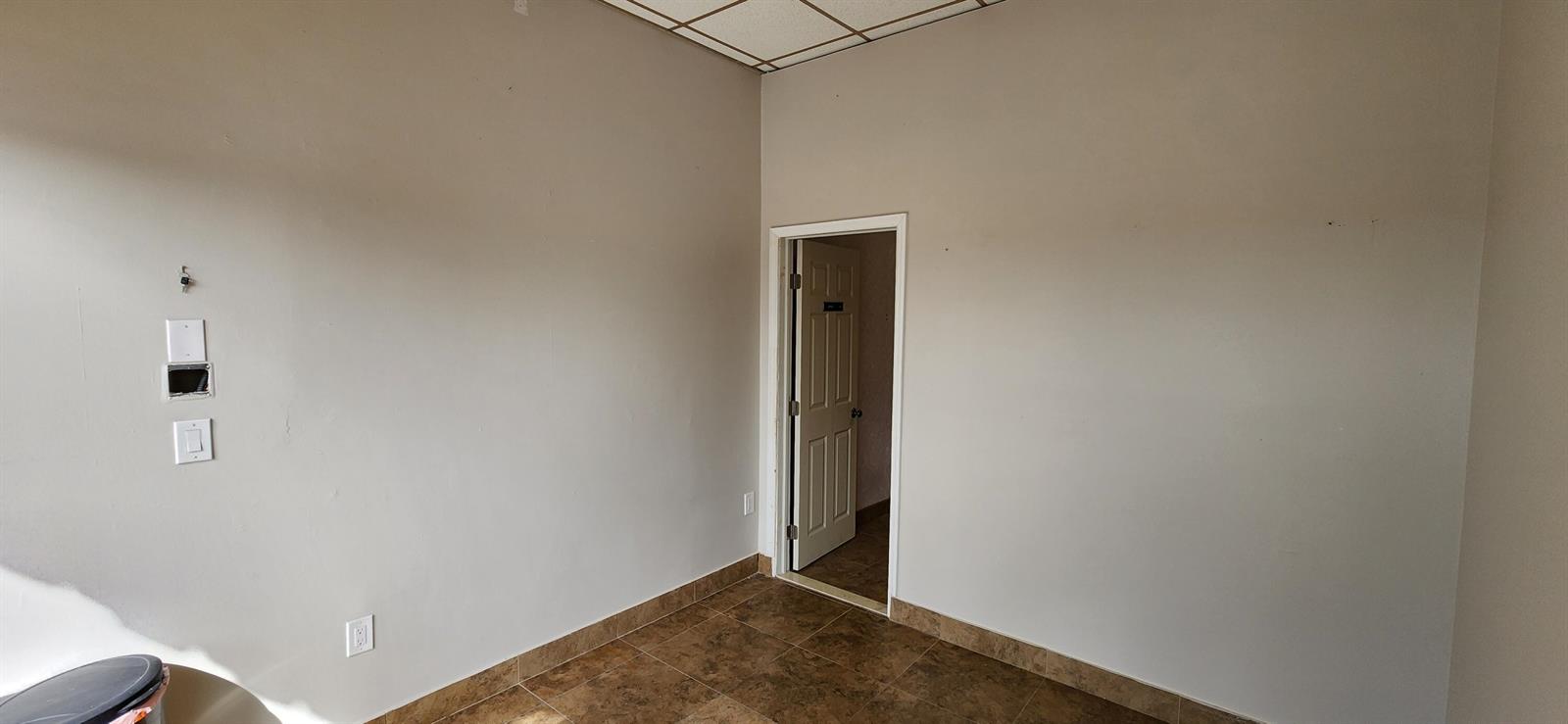 An empty room with beige walls, tile flooring, a drop ceiling, and an open doorway — 1207 S Powerline Road, Pompano Beach FL 33069, POMPANO BEACH, FL