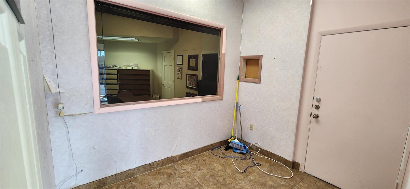 A small room with tiled floors, a large interior window, and a light-colored door — 1207 S Powerline Road, Pompano Beach FL 33069, POMPANO BEACH, FL