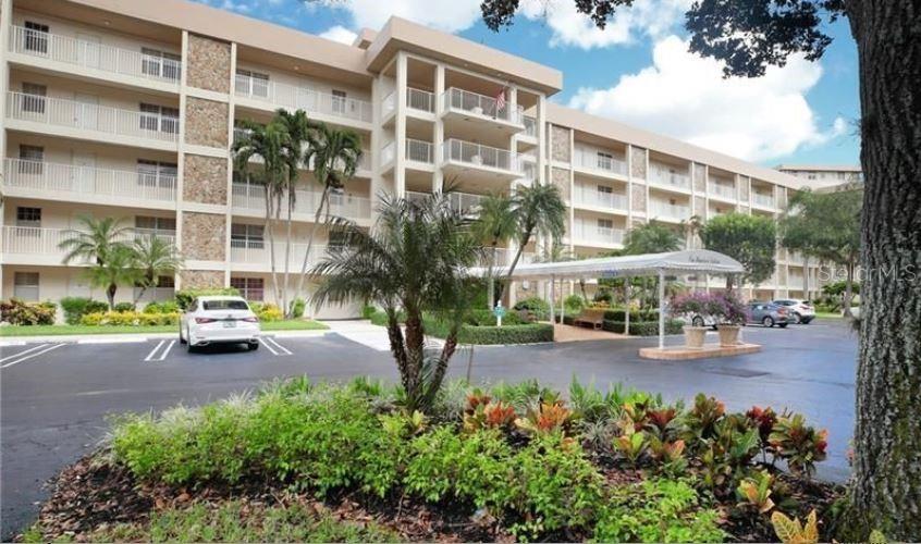 A multi-story apartment building with balconies, palm trees, and a covered entrance in a parking lot — 3503 OAKS WAY UNIT 212, POMPANO BEACH, FL