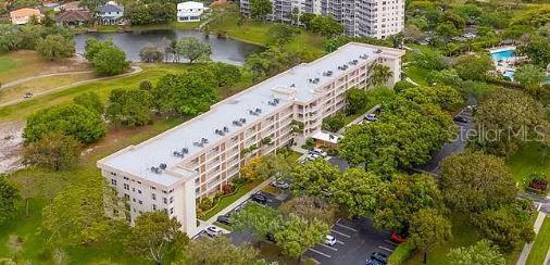 An aerial view shows a multi-story apartment building surrounded by trees, a pond, and parking — 3503 OAKS WAY UNIT 212, POMPANO BEACH, FL