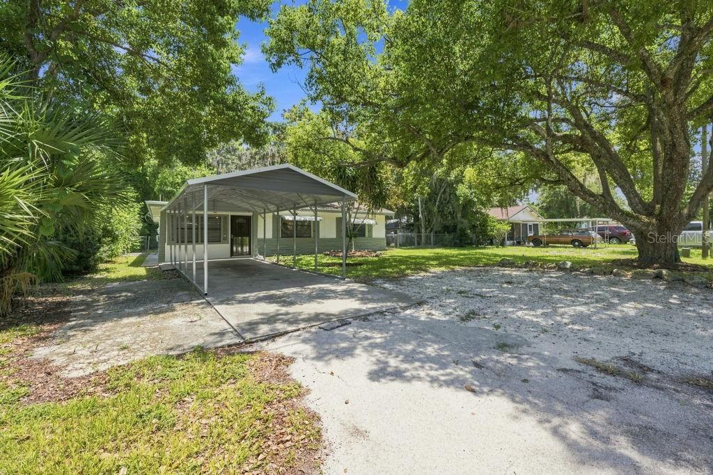 A single-story house with a metal carport and a large tree in the front yard — 7810 CHAPEL AVENUE, PORT RICHEY, FL