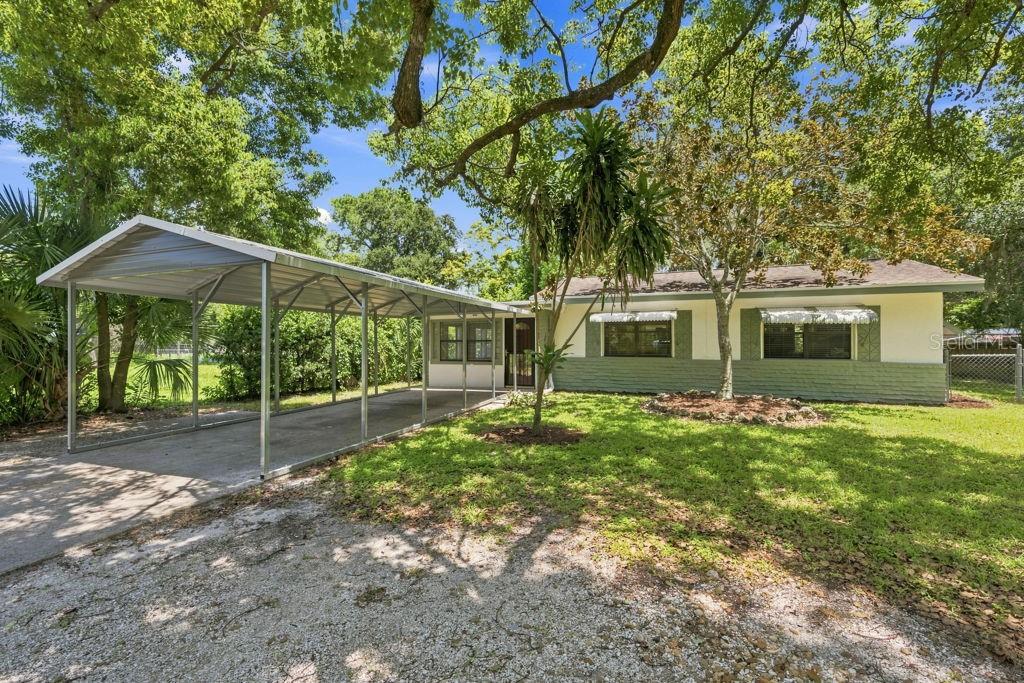 A single-story house with a metal carport, green brick siding, and a large front yard — 7810 CHAPEL AVENUE, PORT RICHEY, FL