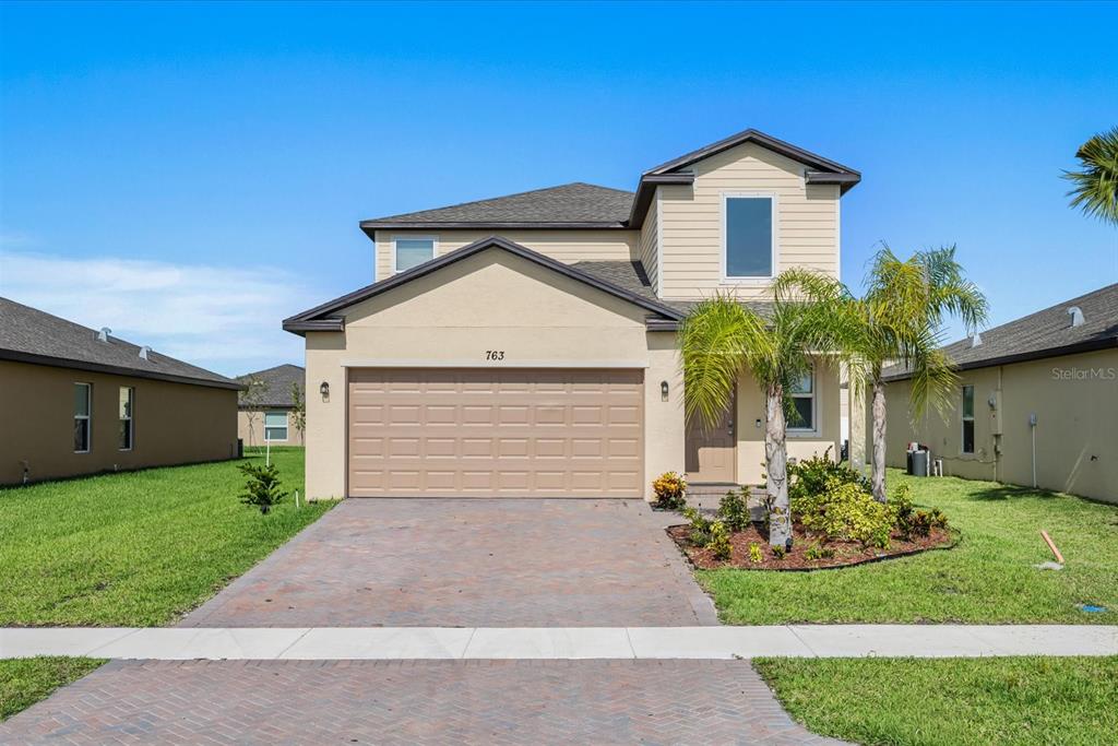 A two-story suburban house features a tan exterior, a two-car garage, and a paved driveway — 763 CARLYLE WAY, FORT PIERCE, FL