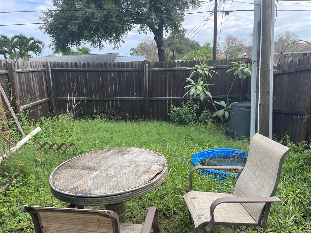 A backyard features a wooden fence, overgrown grass, patio furniture, and a small plastic pool — 639 MICHIGAN BOULEVARD UNIT 1700, DUNEDIN, FL