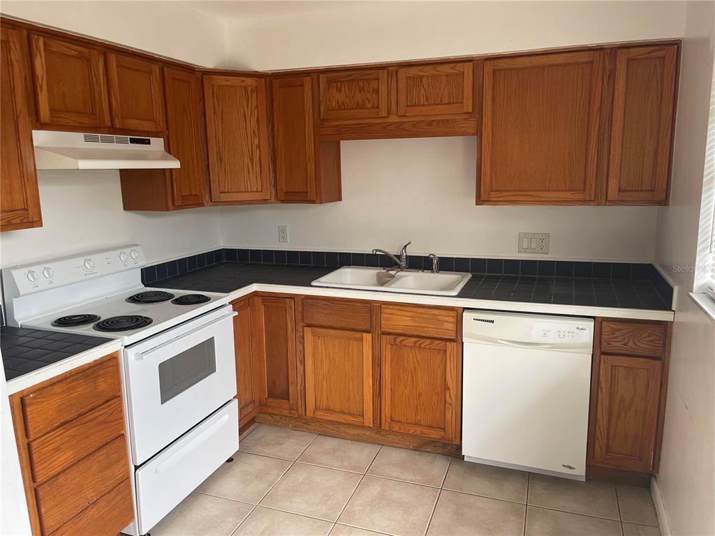 A kitchen with wood cabinets, white appliances, and black tile countertops — 639 MICHIGAN BOULEVARD UNIT 1700, DUNEDIN, FL