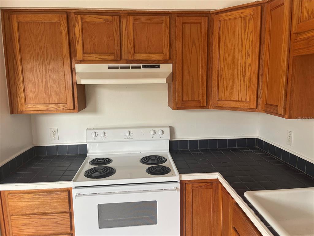 A kitchen features oak cabinets, a white electric stove, and black tiled countertops — 639 MICHIGAN BOULEVARD UNIT 1700, DUNEDIN, FL