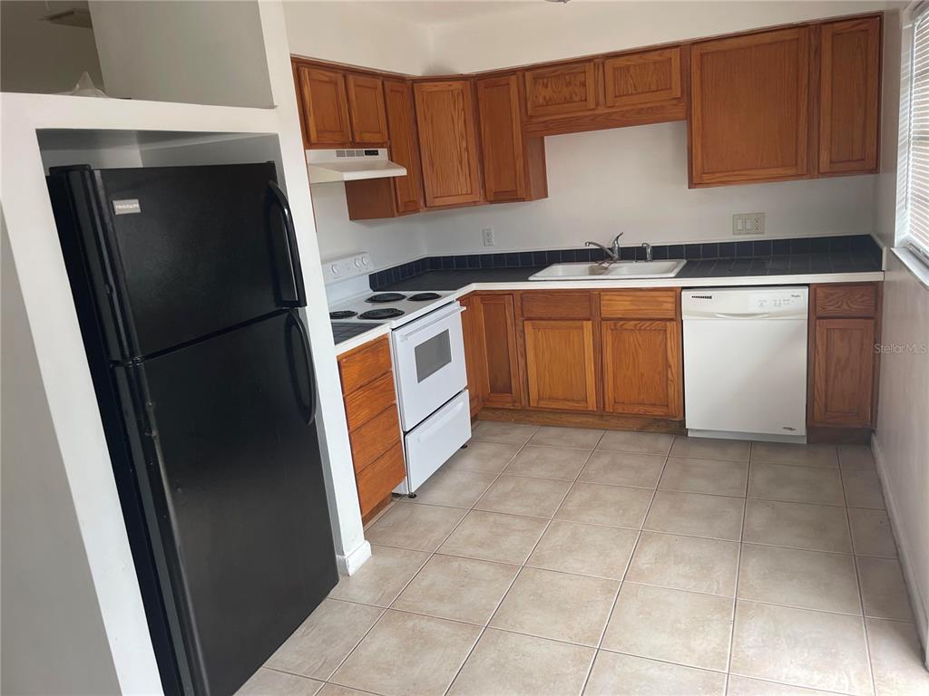 A kitchen features wood cabinets, black and white appliances, tile flooring, and dark countertops — 639 MICHIGAN BOULEVARD UNIT 1700, DUNEDIN, FL