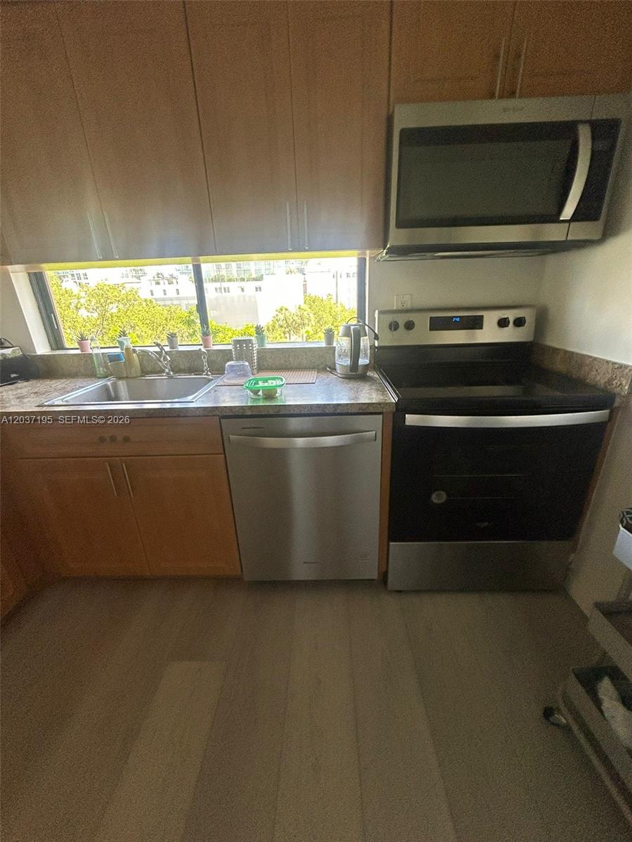 A kitchen features wood cabinets, stainless steel appliances, and a window overlooking city buildings — SUNNY ISLES BEACH, FL