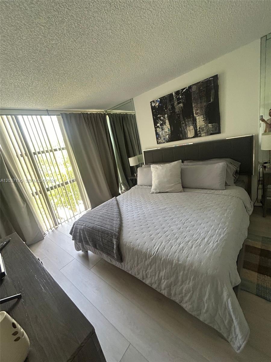 A bedroom features a bed with grey bedding, a dark headboard, and floor-to-ceiling windows — SUNNY ISLES BEACH, FL