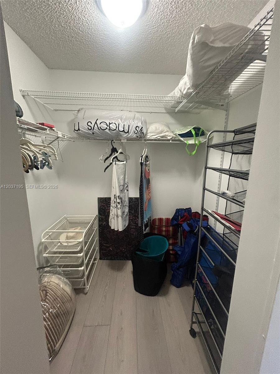 A walk-in closet features wire shelving, a rolling storage rack, and light-colored wood flooring — SUNNY ISLES BEACH, FL