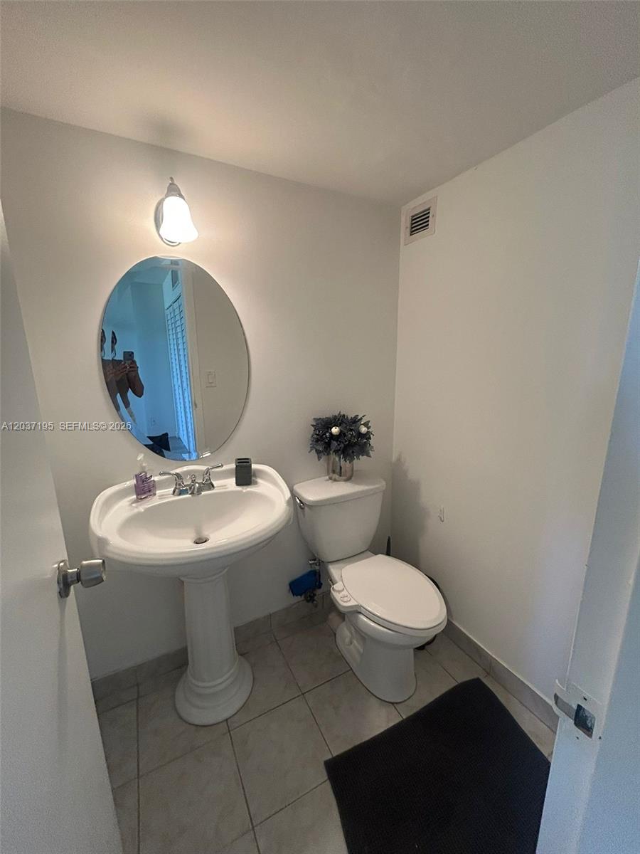 A small bathroom features a pedestal sink, an oval mirror, and a white toilet — SUNNY ISLES BEACH, FL