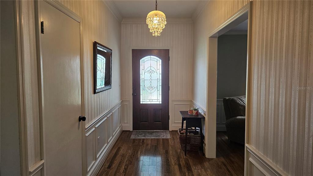 A foyer with wood floors, striped wallpaper, wainscoting, a crystal chandelier, and a front door — 184 LAKE OTIS ROAD, WINTER HAVEN, FL