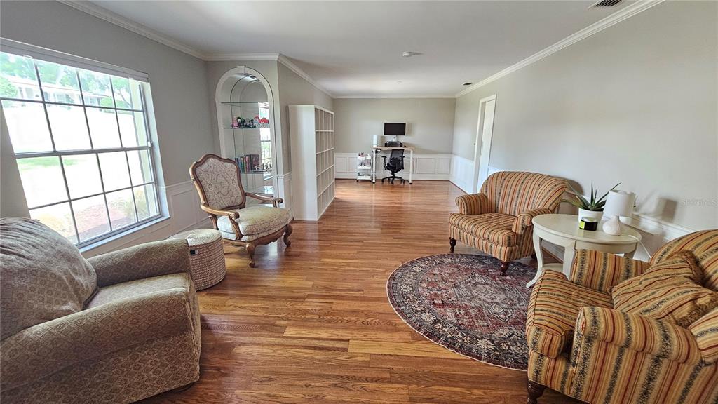 A spacious living room features hardwood floors, multiple armchairs, a desk area, and built-in shelving — 184 LAKE OTIS ROAD, WINTER HAVEN, FL