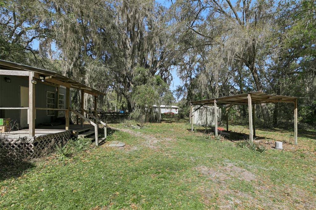 A yard features a small house with a porch and a separate open-sided metal shelter — 15527 TROUSDALE STREET, CLERMONT, FL