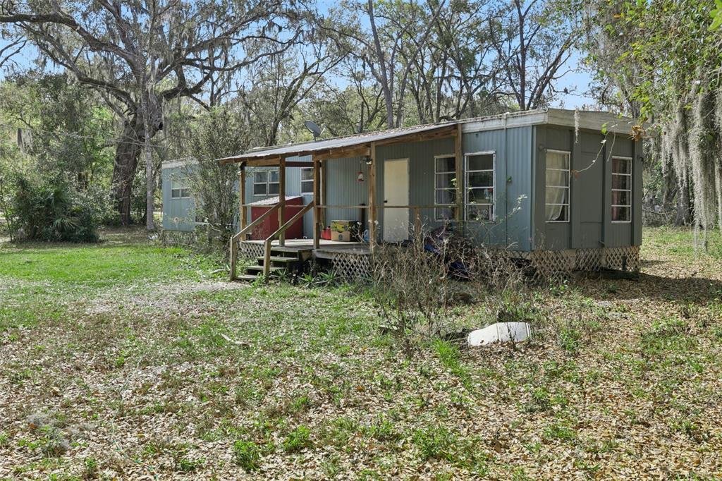 A single-story mobile home with a wooden porch sits on a wooded, leaf-covered lot — 15527 TROUSDALE STREET, CLERMONT, FL