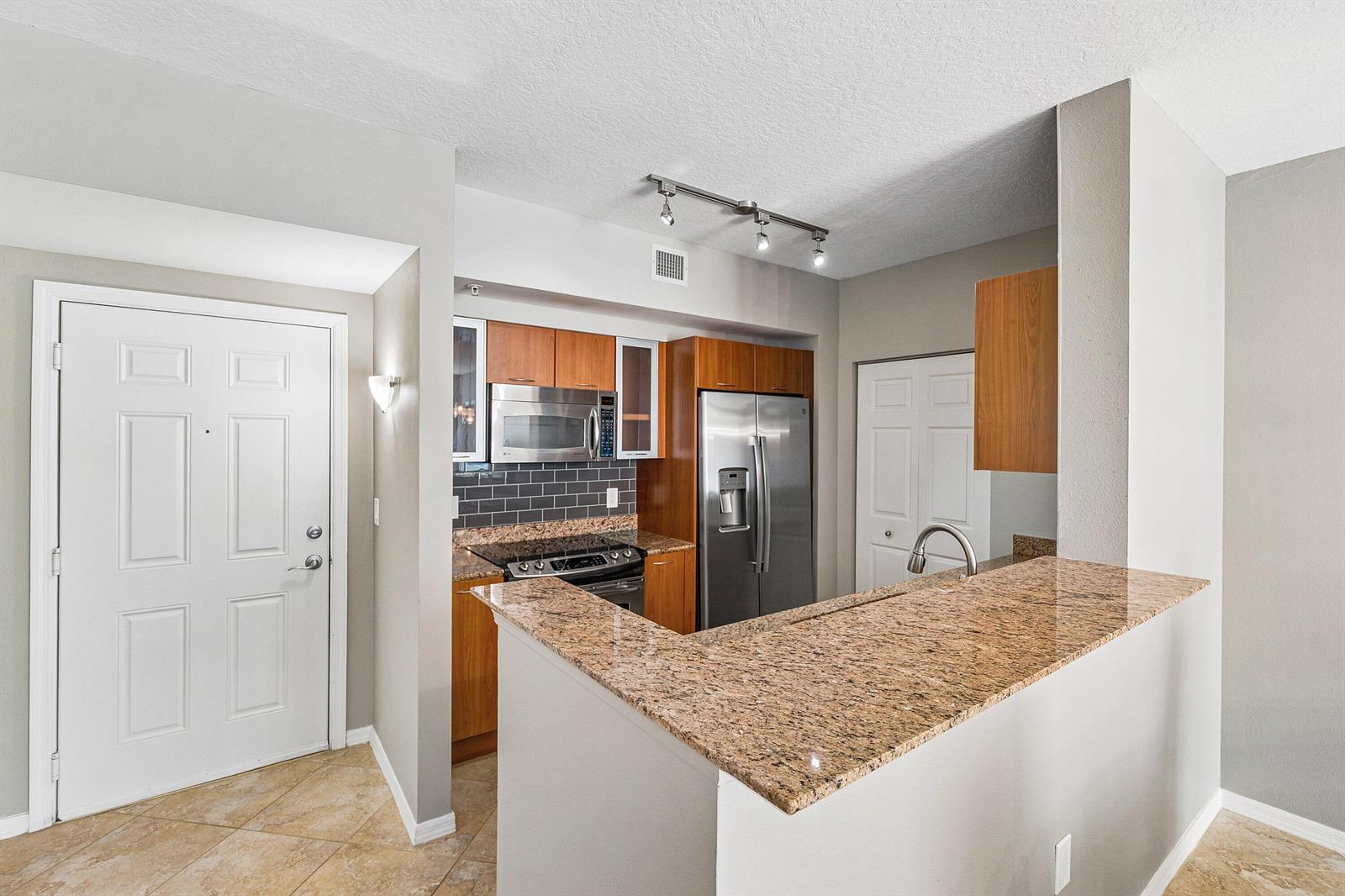 A kitchen with wood cabinets and granite countertops overlooks a living room with balcony access — 700 E Boynton Beach Boulevard # 803, Boynton Beach FL 33435, BOYNTON BEACH, FL