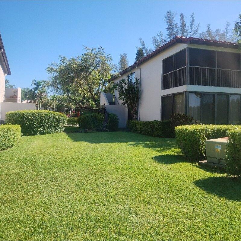 A two-story building with screened balconies sits behind a manicured lawn and green hedges — 21535 Cypress Hammock Drive # 36j, Boca Raton FL 33428, BOCA RATON, FL