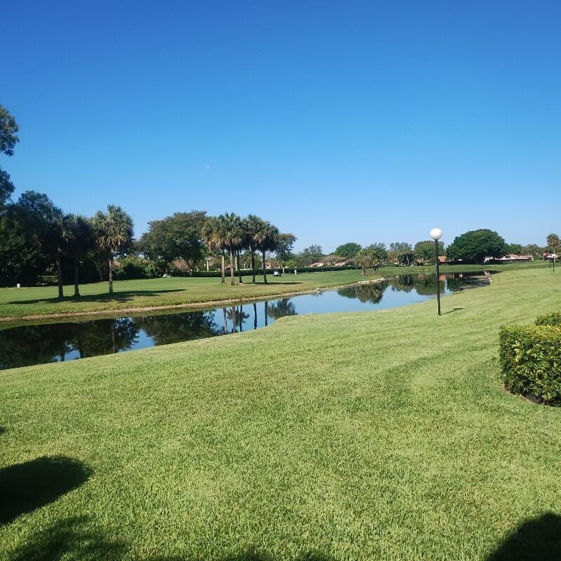 A grassy lawn leads to a pond with palm trees and a clear blue sky — 21535 Cypress Hammock Drive # 36j, Boca Raton FL 33428, BOCA RATON, FL