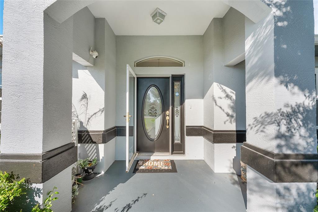 A covered entryway features a dark front door with an oval glass insert and sidelight — 8601 SW 60TH CIRCLE, OCALA, FL