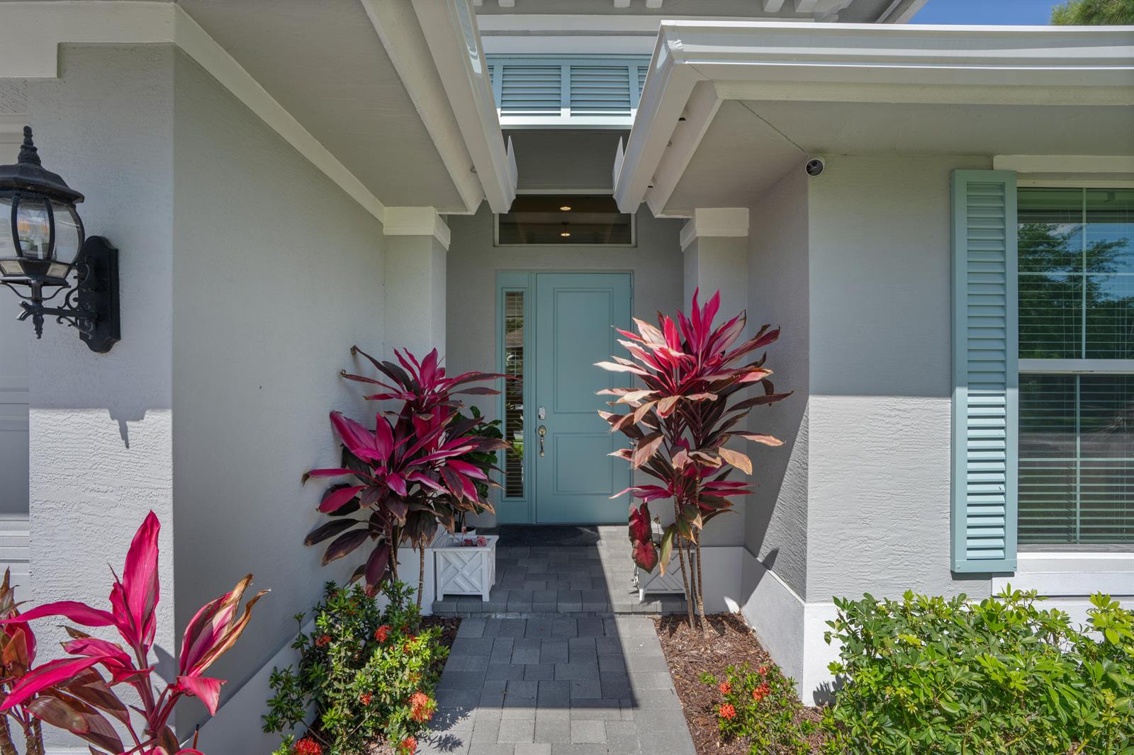 The exterior entrance features a light blue door, gray stucco walls, and vibrant red plants — 6805 49th Court, Vero Beach FL 32967, VERO BEACH, FL