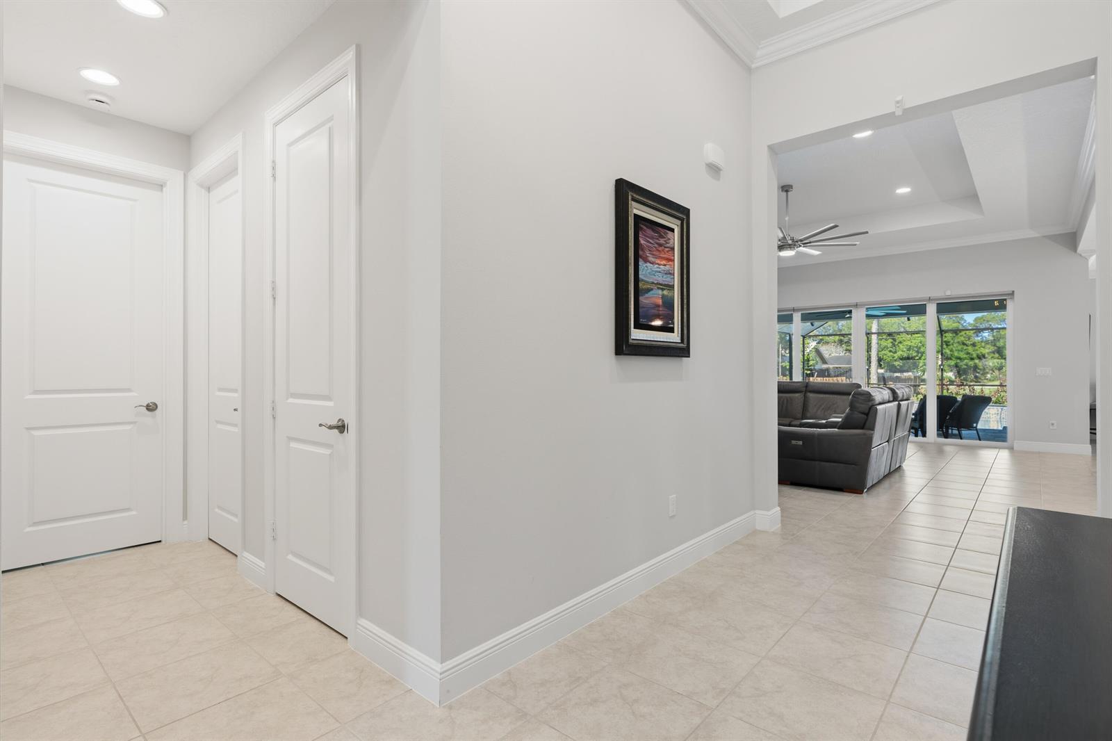 A hallway with white doors leads to a living room with tile floors and ceiling fans — 6805 49th Court, Vero Beach FL 32967, VERO BEACH, FL