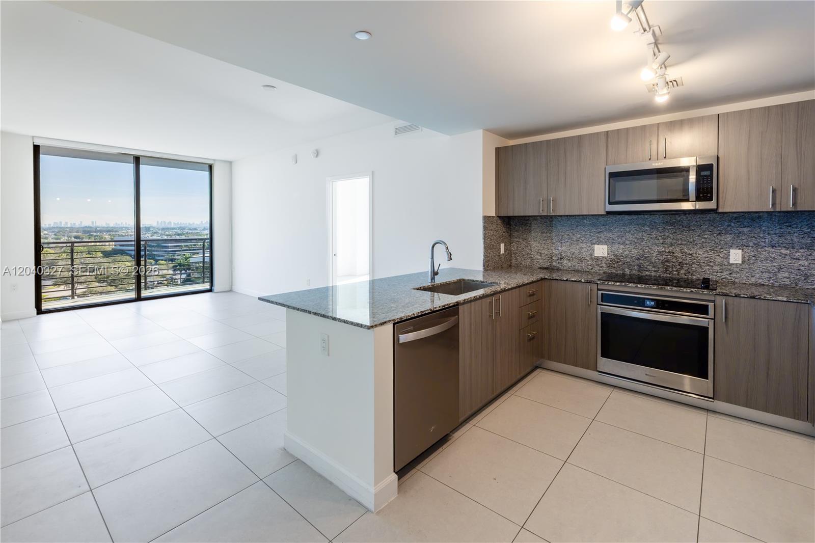 A modern kitchen with wood-tone cabinets and granite countertops opens to a bright living area — 5350 NW 84th Ave # 1001, Doral FL 33166, DORAL, FL