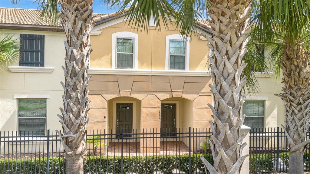 A two-story townhouse exterior features tan stucco walls, dark doors, and a black metal fence — 1987 MAJORCA DRIVE, KISSIMMEE, FL