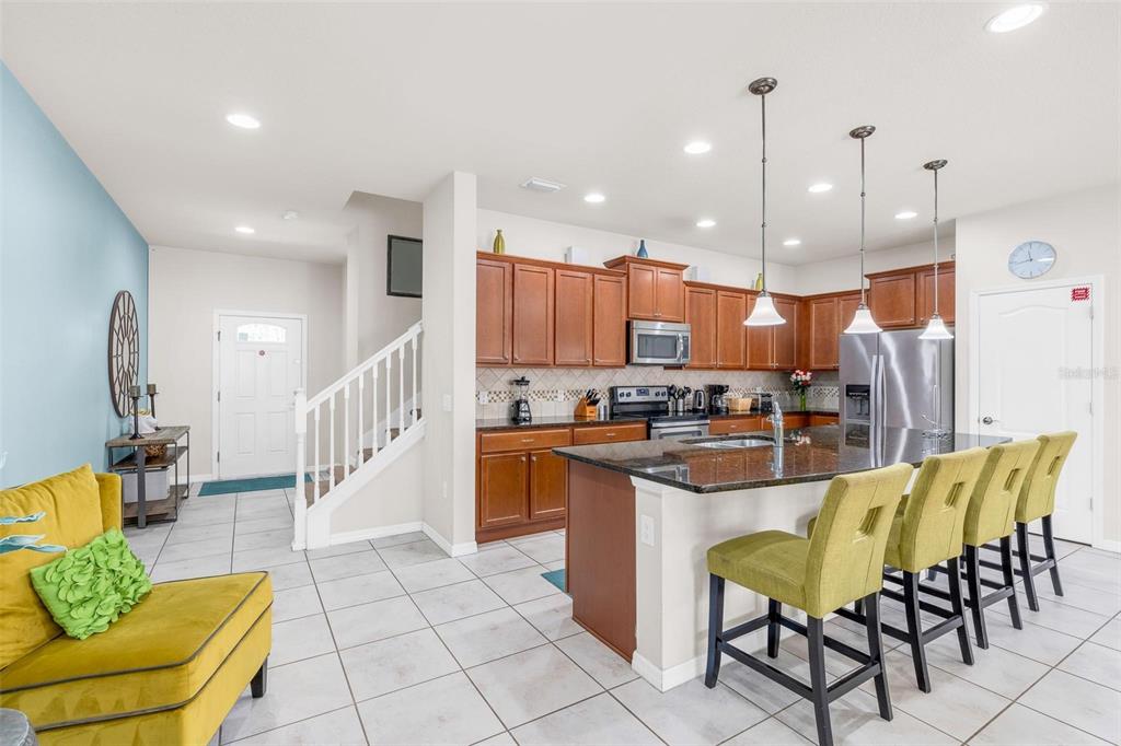 A kitchen with wood cabinets and a granite island overlooks a living area with tile — 1987 MAJORCA DRIVE, KISSIMMEE, FL