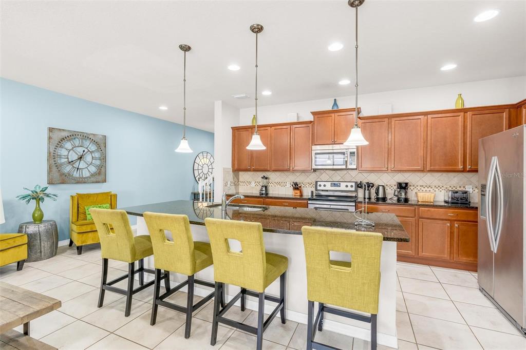 A kitchen features wood cabinets, granite countertops, a breakfast bar with yellow chairs, and pendants — 1987 MAJORCA DRIVE, KISSIMMEE, FL