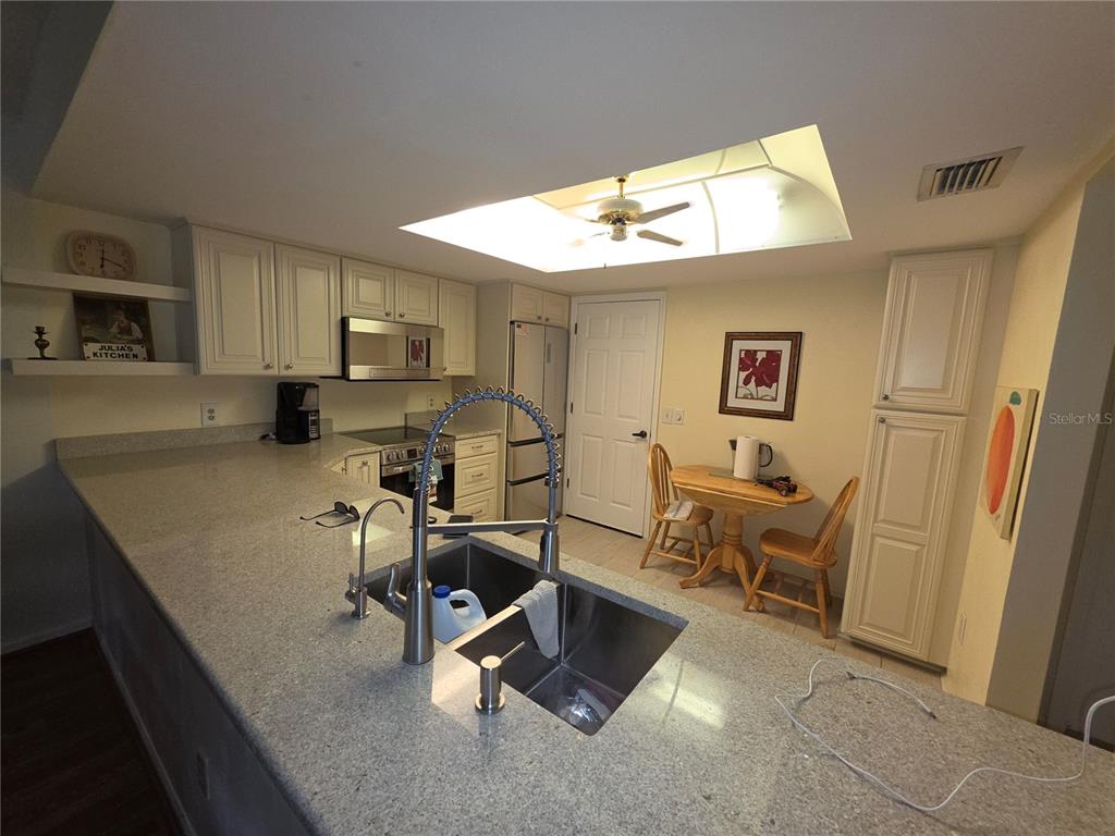 A kitchen features light-colored cabinetry, granite countertops, a double sink, and a small dining area — 18427 AINTREE COURT, TAMPA, FL