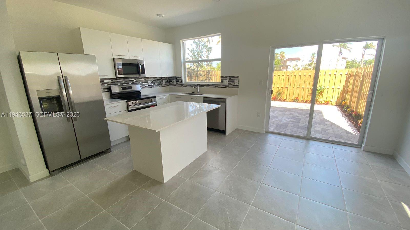 A modern kitchen features white cabinetry, stainless steel appliances, a center island, and sliding doors — 12075 NW 24th Ct, Miami FL 33167, MIAMI, FL