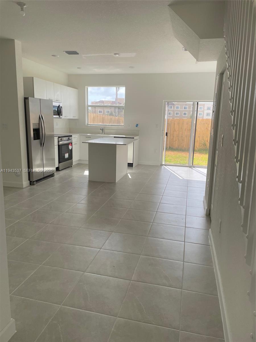 A kitchen with white cabinets, stainless steel appliances, a center island, and tile flooring — 12075 NW 24th Ct, Miami FL 33167, MIAMI, FL