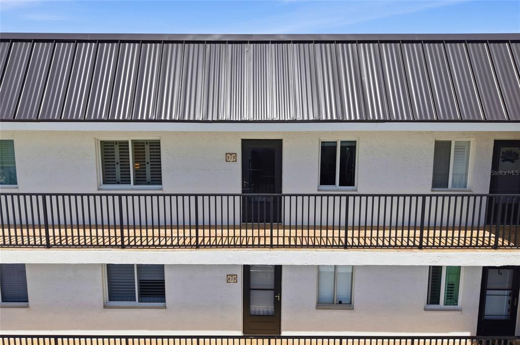 An exterior view of a two-story apartment building with white stucco walls and metal roofing — 8977 MIDNIGHT PASS ROAD UNIT 519, SARASOTA, FL