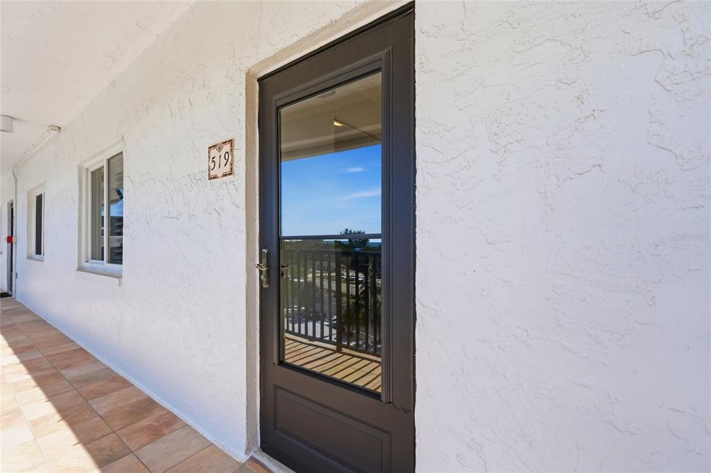 A dark-framed storm door with a number plate sits on a white stucco exterior walkway — 8977 MIDNIGHT PASS ROAD UNIT 519, SARASOTA, FL