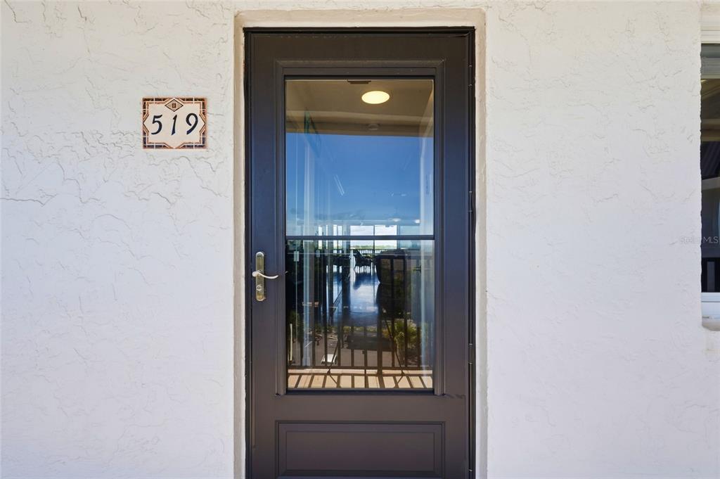 A dark-framed glass storm door is mounted on a white stucco wall next to address 519 — 8977 MIDNIGHT PASS ROAD UNIT 519, SARASOTA, FL