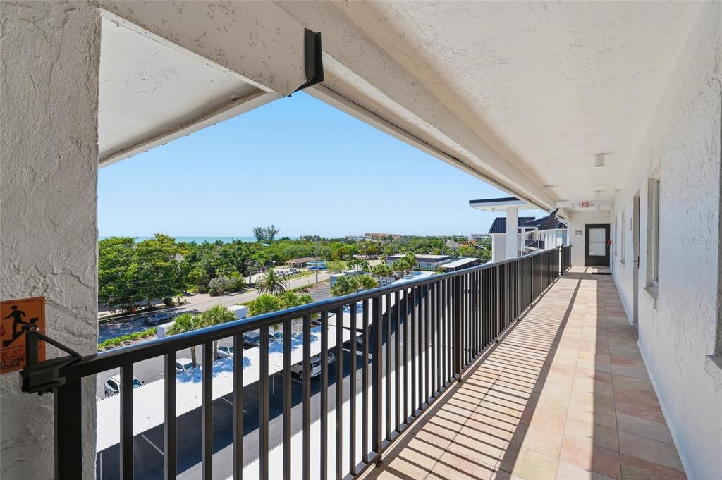 An outdoor balcony with a black metal railing overlooks a parking lot and the ocean — 8977 MIDNIGHT PASS ROAD UNIT 519, SARASOTA, FL