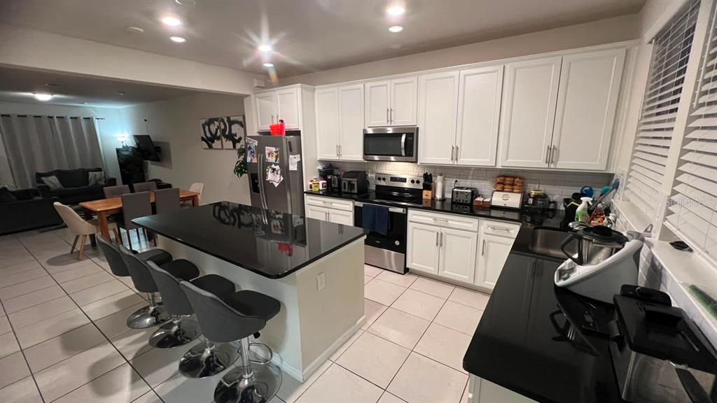 A kitchen features white cabinets, black countertops, a central island with bar stools, and tile flooring — 14339 SAPELO BEACH DRIVE, ORLANDO, FL