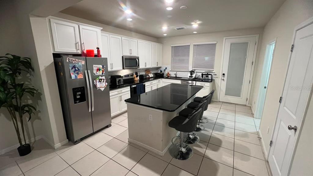 A kitchen features white cabinets, black countertops, a central island with bar stools, and tile flooring — 14339 SAPELO BEACH DRIVE, ORLANDO, FL