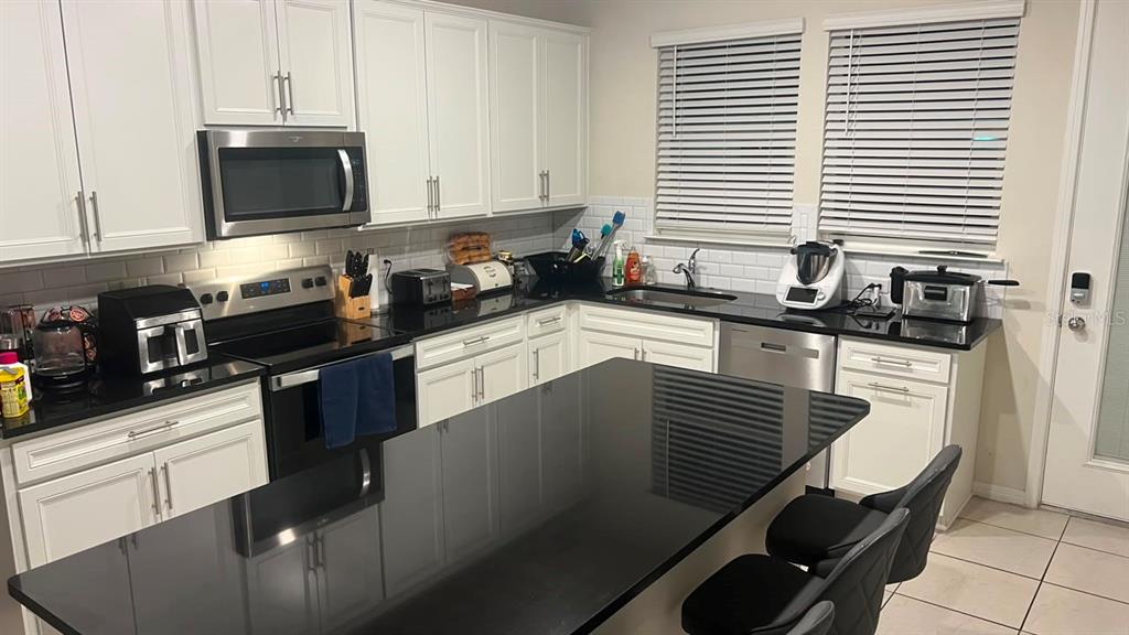 A kitchen features white cabinets, black countertops, a central island, and stainless steel appliances — 14339 SAPELO BEACH DRIVE, ORLANDO, FL