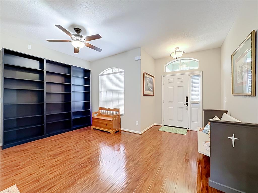 A room with wood flooring, a large black bookshelf, a wooden bench, and an entryway — 6161 BOBBY JONES COURT, PALMETTO, FL