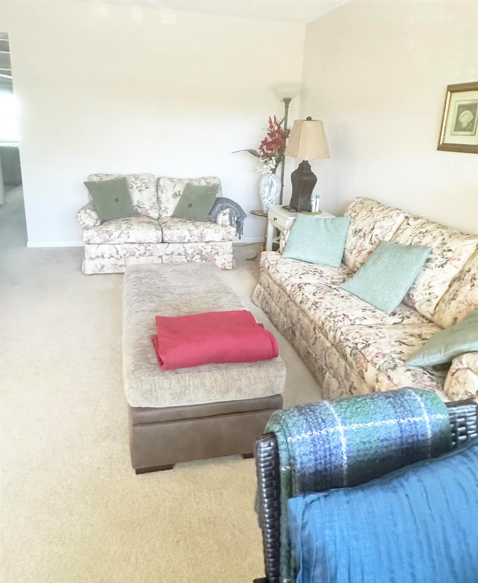 A living room features floral sofas, a large ottoman with a pink throw, and carpeting — 3097 Newport S # 3097, Deerfield Beach FL 33442, DEERFIELD BEACH, FL