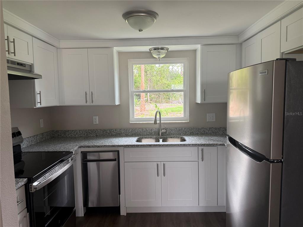 A kitchen featuring white cabinets, granite countertops, stainless steel appliances, and a window above the sink — 7335 NEW YORK AVENUE, HUDSON, FL
