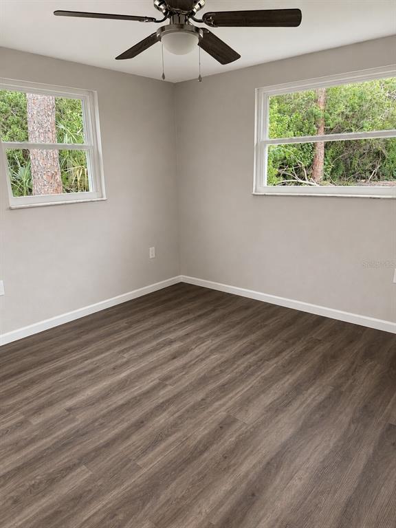 An empty bedroom features light gray walls, dark wood-look flooring, and a ceiling fan — 7335 NEW YORK AVENUE, HUDSON, FL