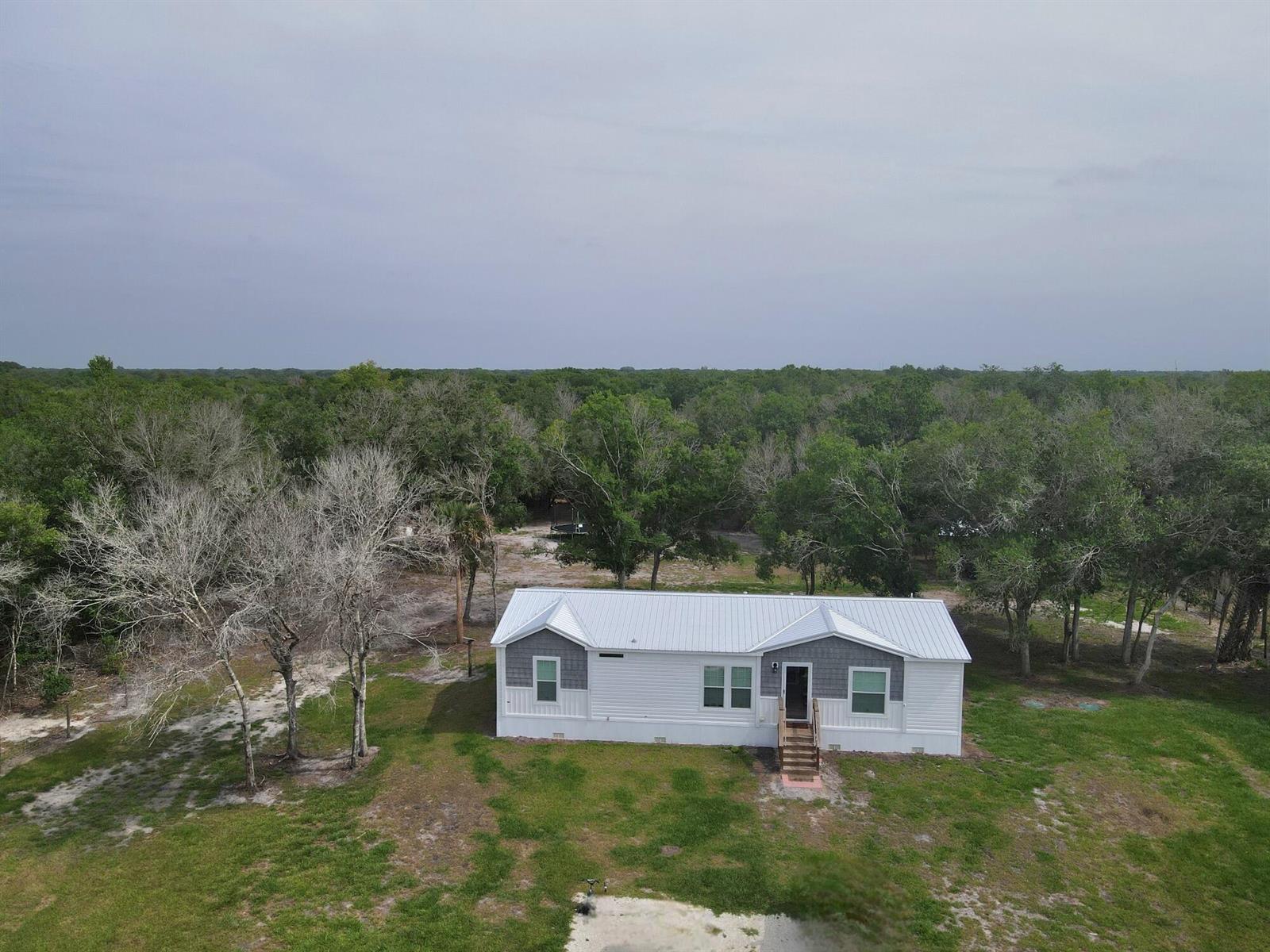 An aerial view shows a white manufactured home with a metal roof and gray accents — 19411 NW 258th Street, Okeechobee FL 34972, OKEECHOBEE, FL
