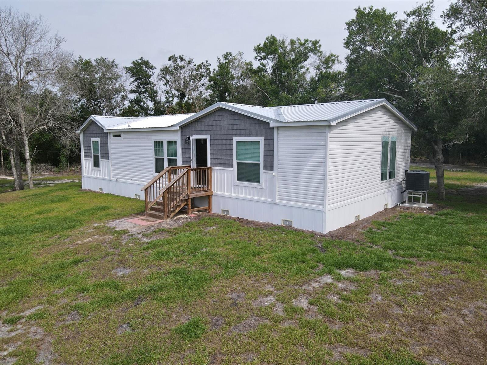 A single-story manufactured home with light siding, a gray accent wall, and wooden stairs — 19411 NW 258th Street, Okeechobee FL 34972, OKEECHOBEE, FL