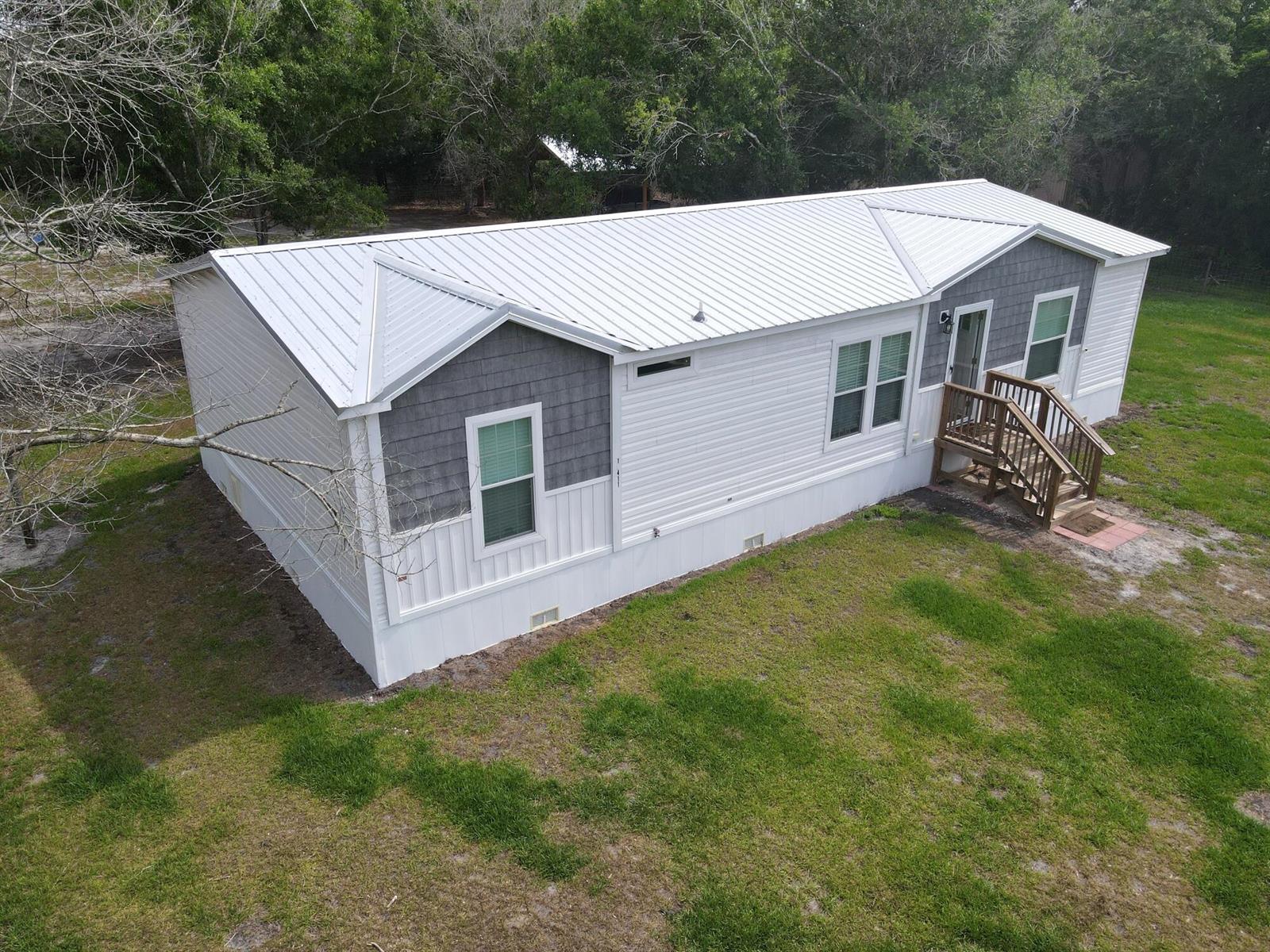 An elevated exterior view of a white manufactured home with a metal roof and deck — 19411 NW 258th Street, Okeechobee FL 34972, OKEECHOBEE, FL