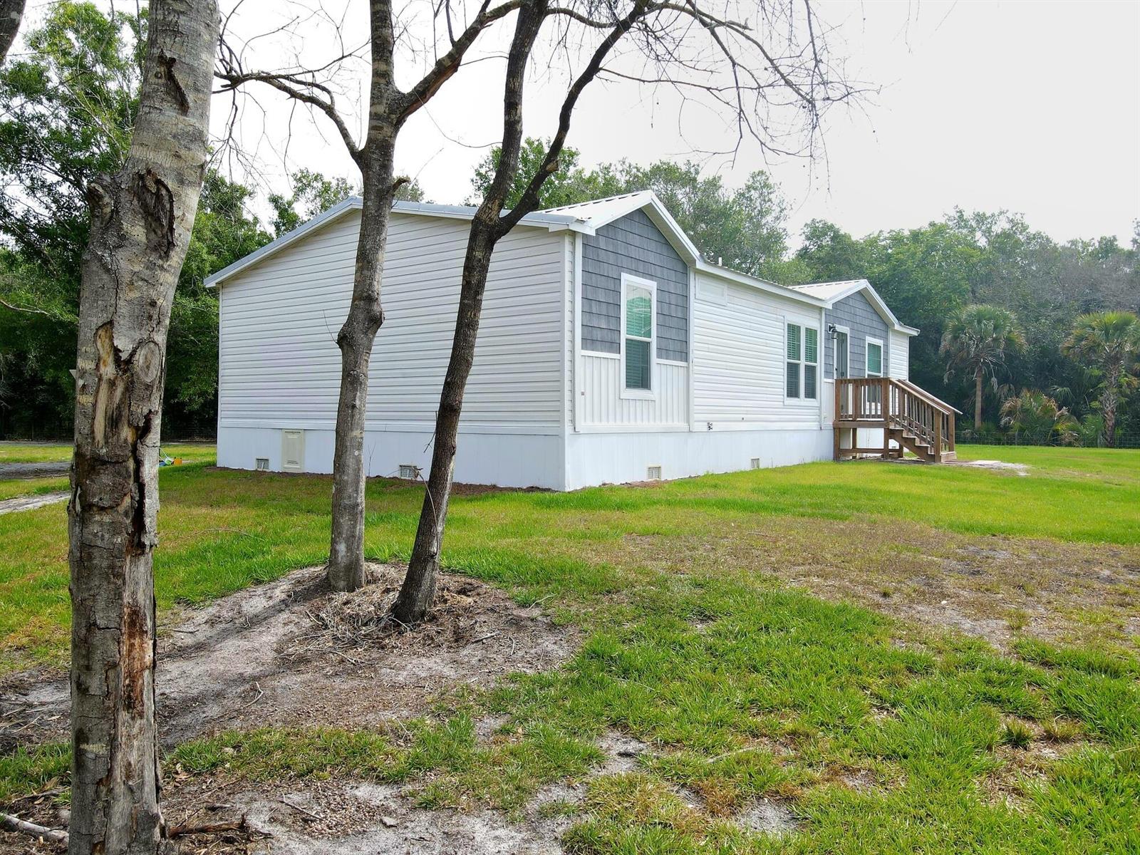 A light-colored manufactured home with gray accent siding sits on a grassy lot — 19411 NW 258th Street, Okeechobee FL 34972, OKEECHOBEE, FL